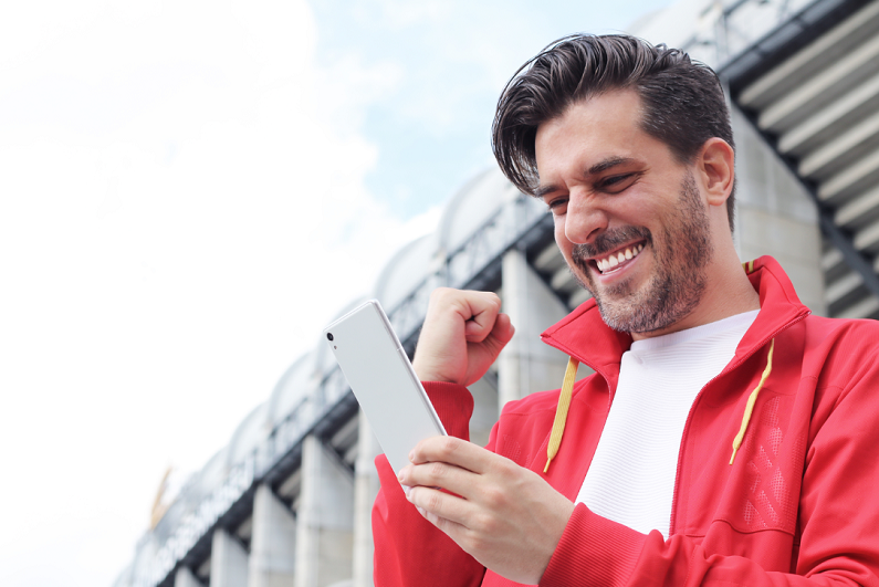 man celebrating winning a bet as he looks at his smartphone